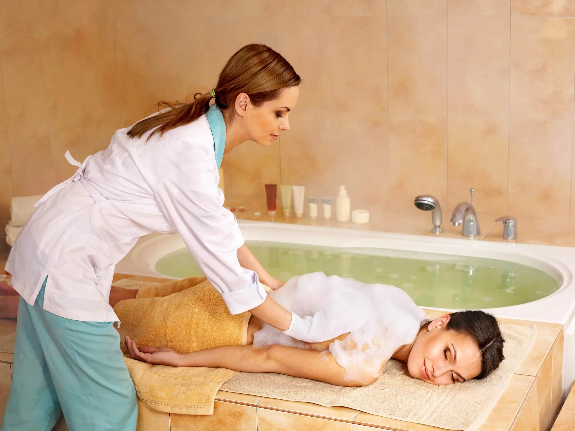 10 Best Spas in Vancouver You Should Never Miss A lady lying near a bath tub and taking Hammam. A masseuse giving the massage to the lady.