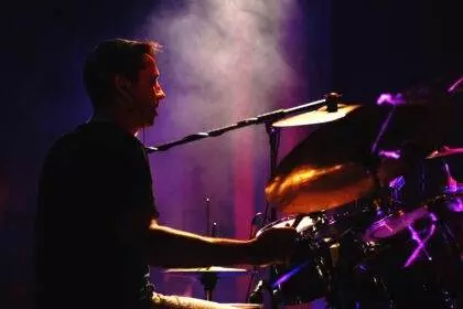 A person playing drums in darkness with a glimpse of light. A musical event is organized by Candlelight featuring the Birth of Soul.