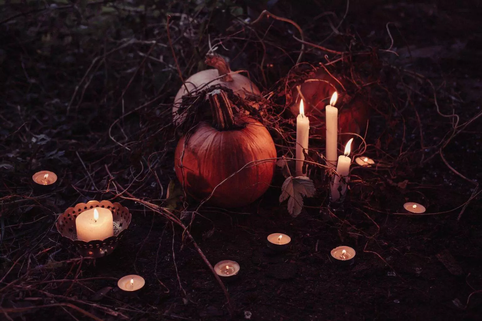 An image of a pumpkin wrapped with tree trunks and various candles lit around it in a dark atmosphere. A Musical Eve of Candlelight featuring Halloween Classics is organized in Ottawa.