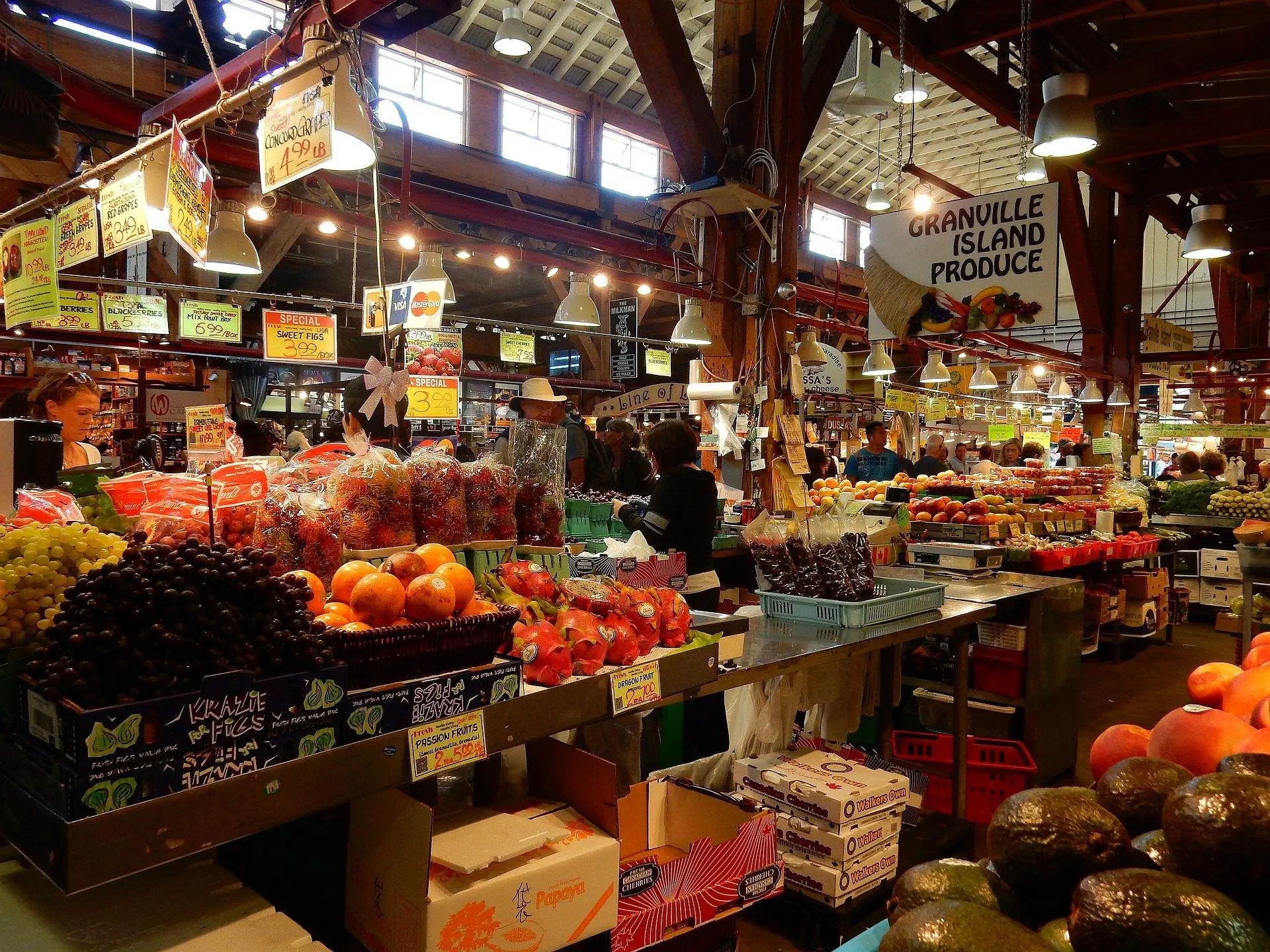 10 Most Popular Places to Visit in Vancouver A view from the Granville Island Public Market visit in Vancouver. A picture of fruits and other grocery shops and people buying them.