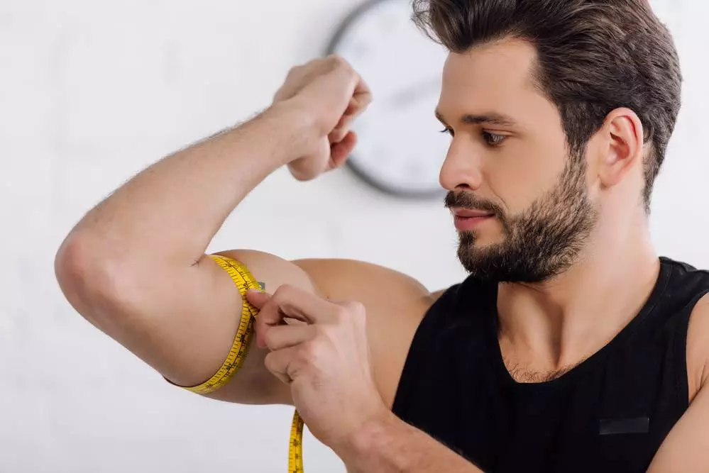 A man measuring his muscles with a measuring tape to check muscle growth.