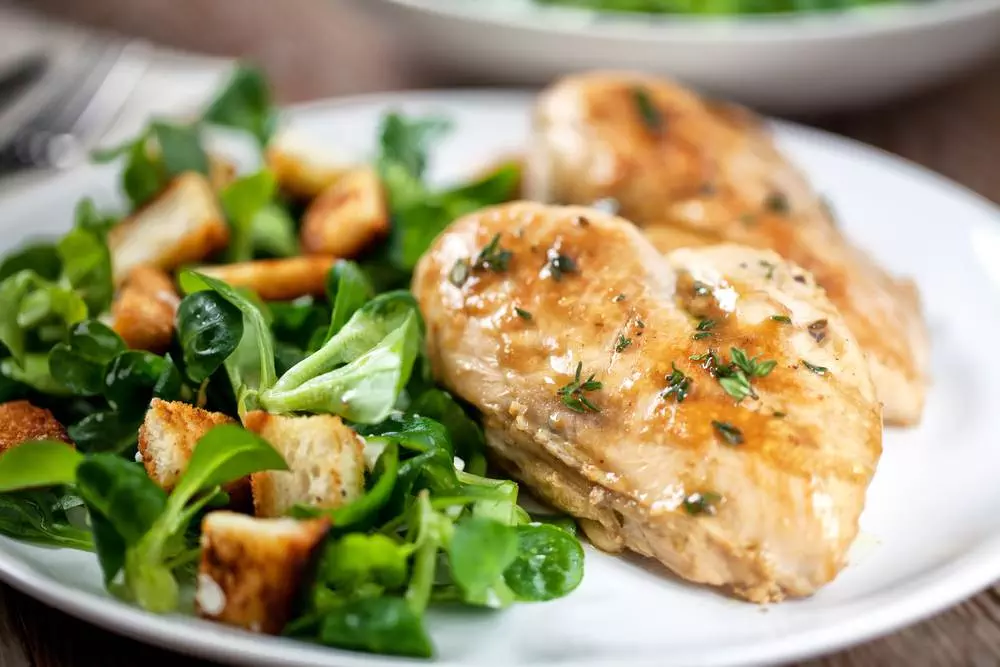 A close-up of a plate with grilled chicken and some green vegetables served together. Is chicken good for health?