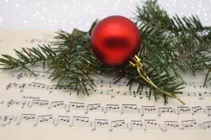 A picture of a Christmas tree leaf and a red Christmas ball lying together on a musical note.