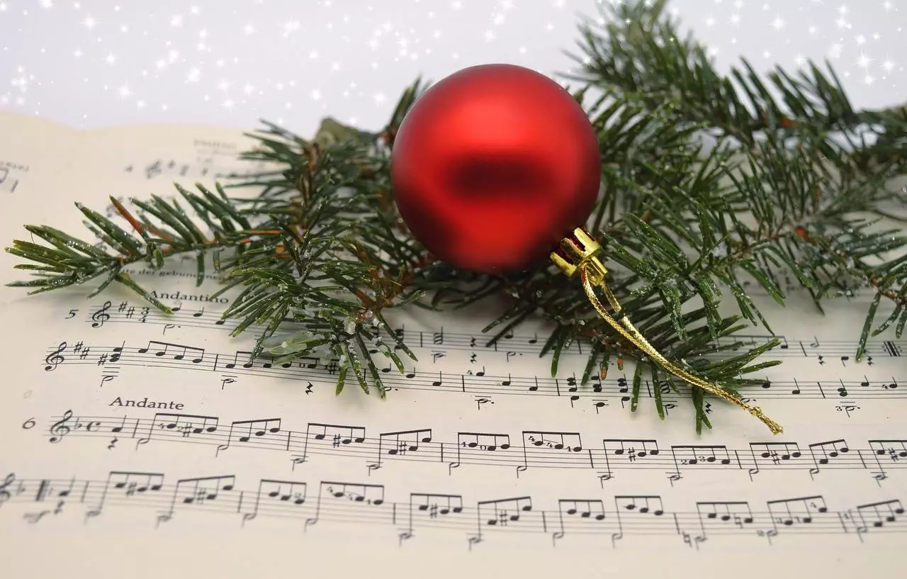 A picture of a Christmas tree leaf and a red Christmas ball lying together on a musical note.