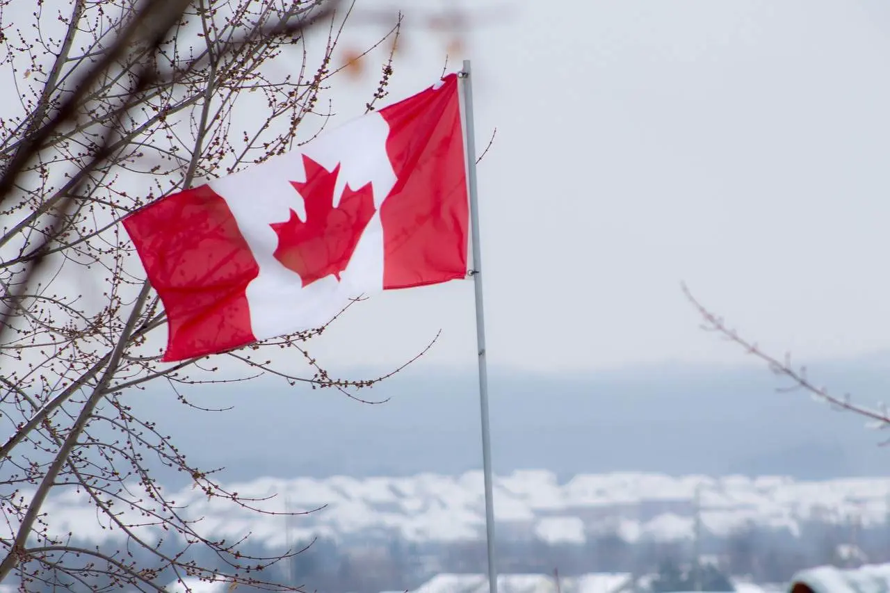 The 12 Best Mountain Ranges in Canada Canada Flag flowing in the air in snowy weather.