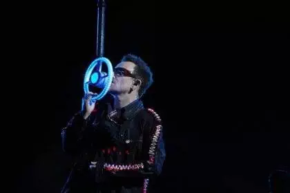 A person wearing sunglasses and singing on a neon mic in dark background.