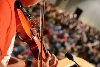 A close-up of a person playing violin and performing in front of the audience. There will be an event of Candlelight