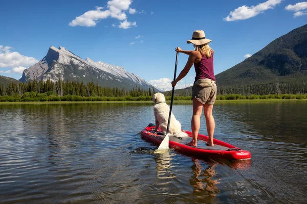 A woman Paddling a boat with her dog sitting in front of Lake Louise.