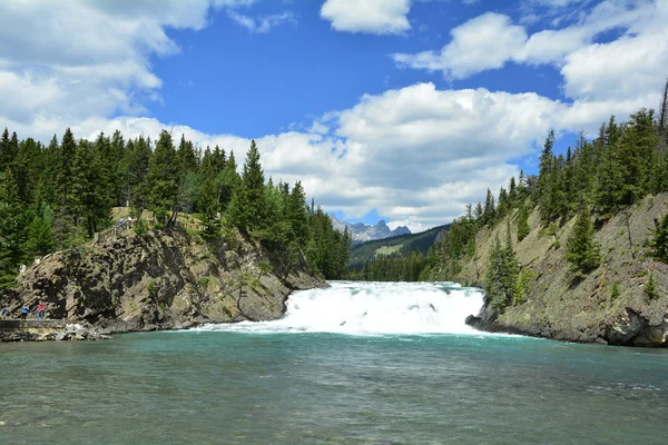 A view of Bow Falls with trees and rocks around it during the daytime.