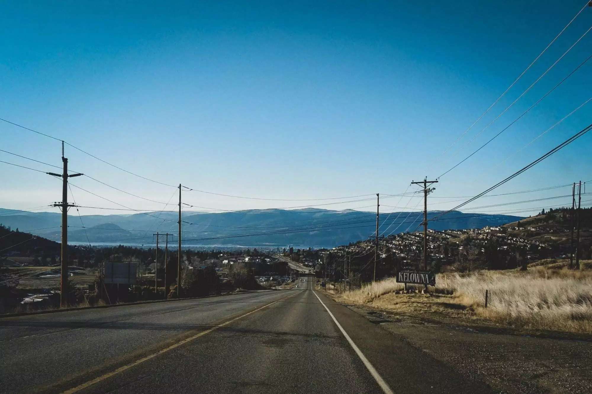 A highway goes towards the Kelowna mountains with Okanagan Lake in the distance.