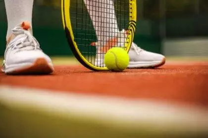 A close-up of a tennis ball on the ground and the racket touching the ground before a match.